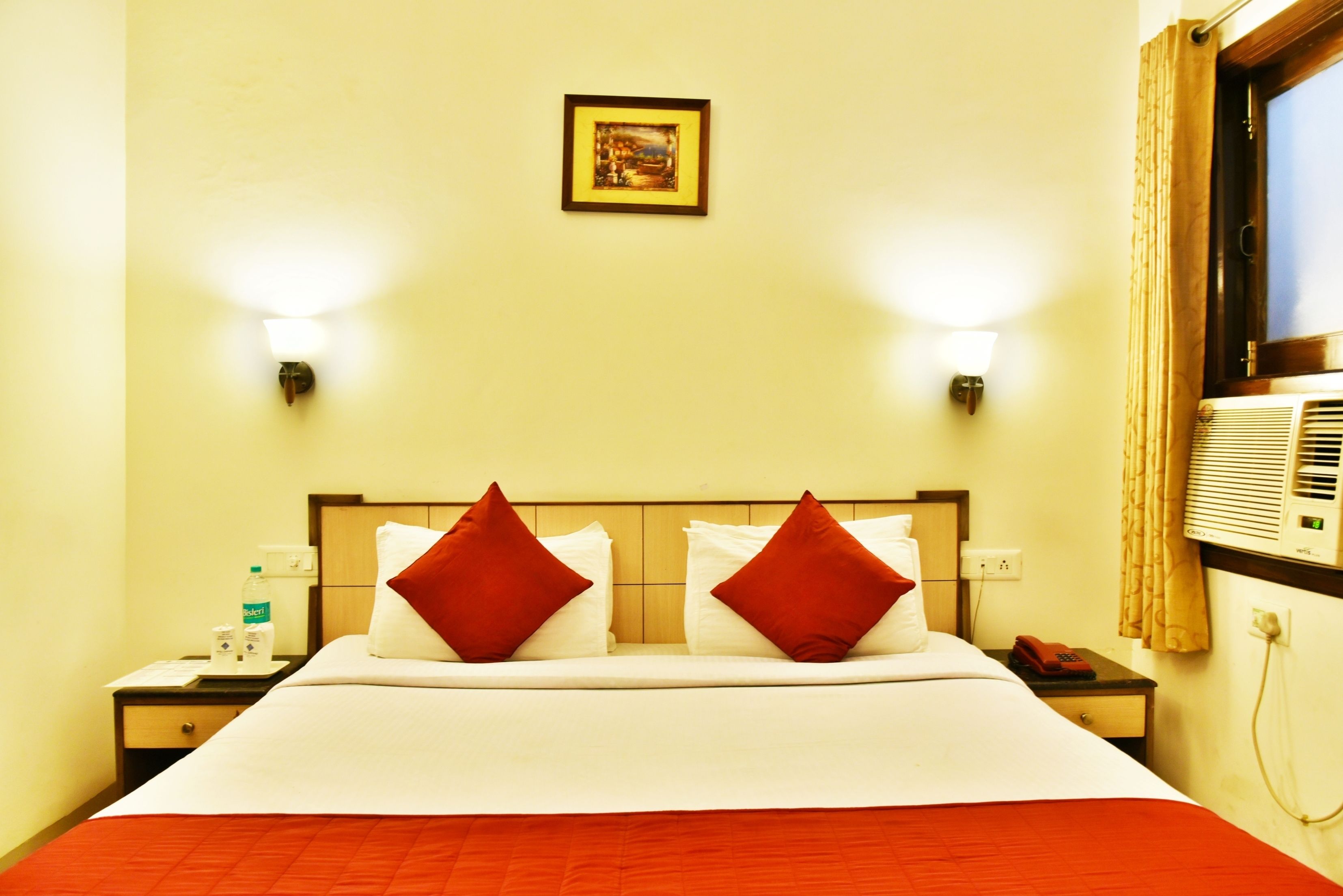 Habitación de hotel con cama, dos mesitas de noche, una lámpara de noche, un cuadro en la pared y una ventana con cortinas.