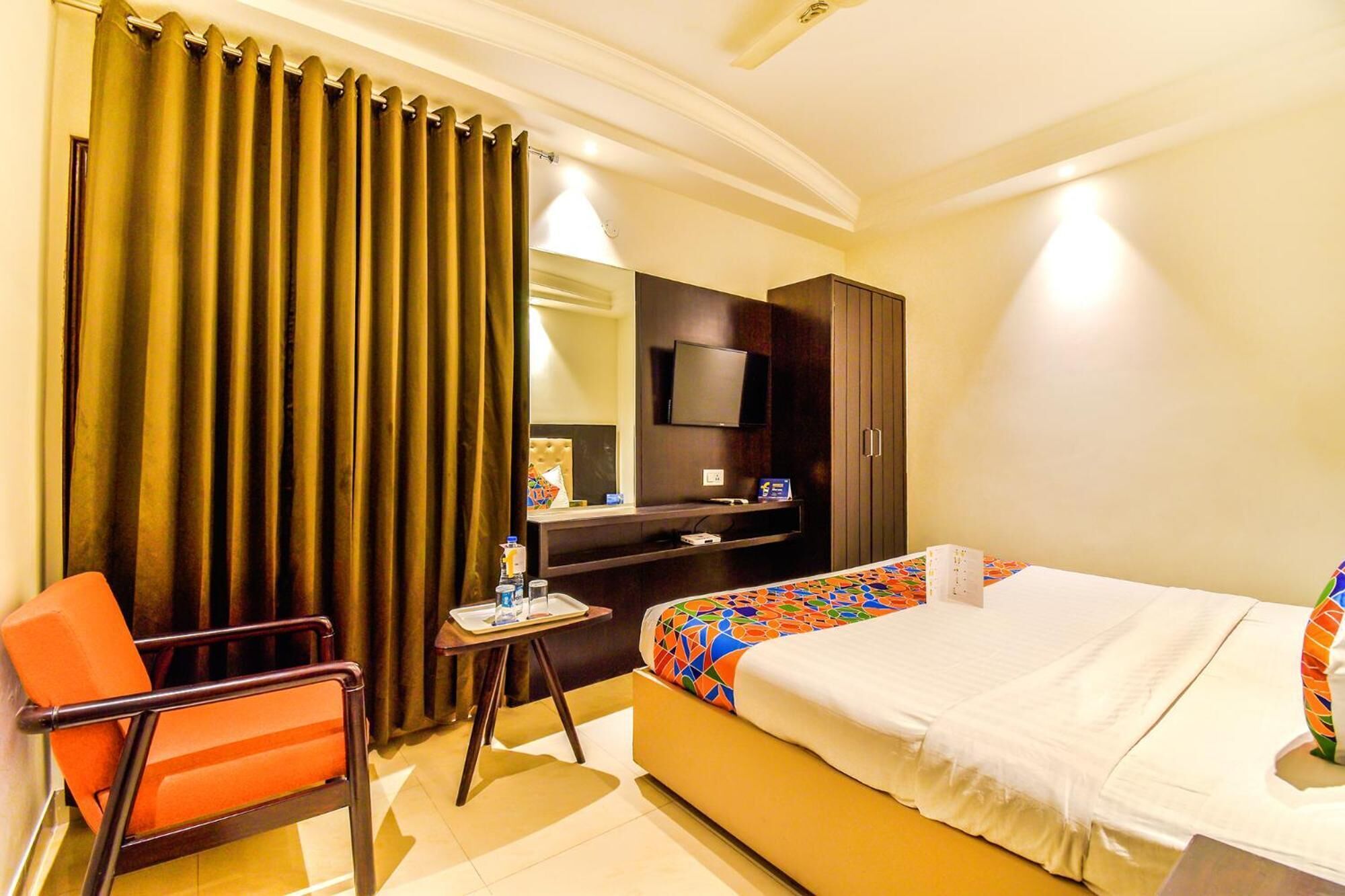 A hotel room with a bed, a desk with a chair, a television, and a large window with curtains.