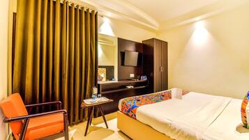 A hotel room with a bed, a desk with a chair, a television, and a large window with curtains.