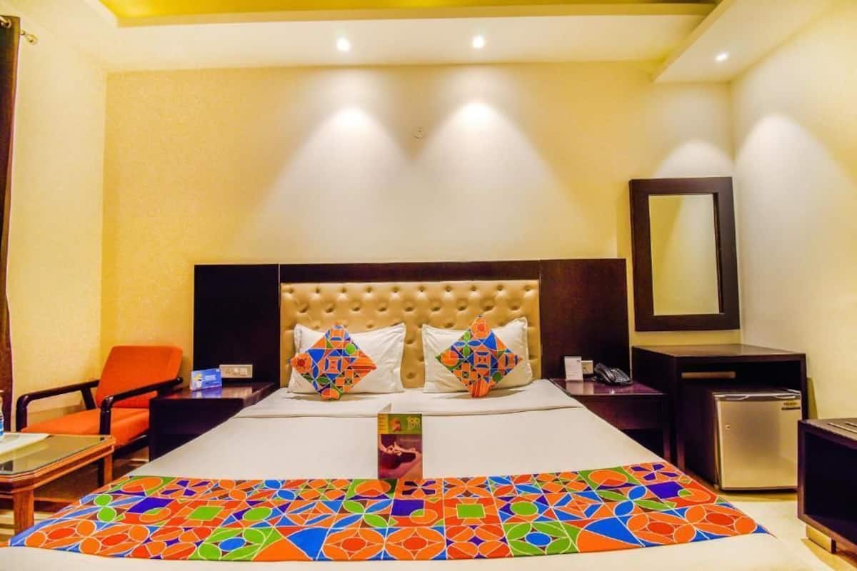 A hotel room with a large bed, a headboard, a bedside table, a chair, a desk, a mirror, and a small refrigerator.