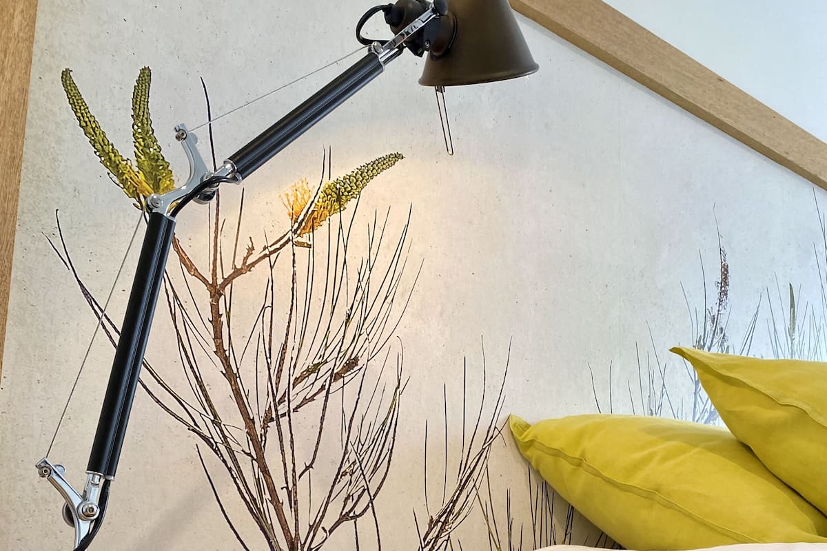 A wooden bedside table with a desk lamp, a bed with white bedding, and a yellow pillow.
