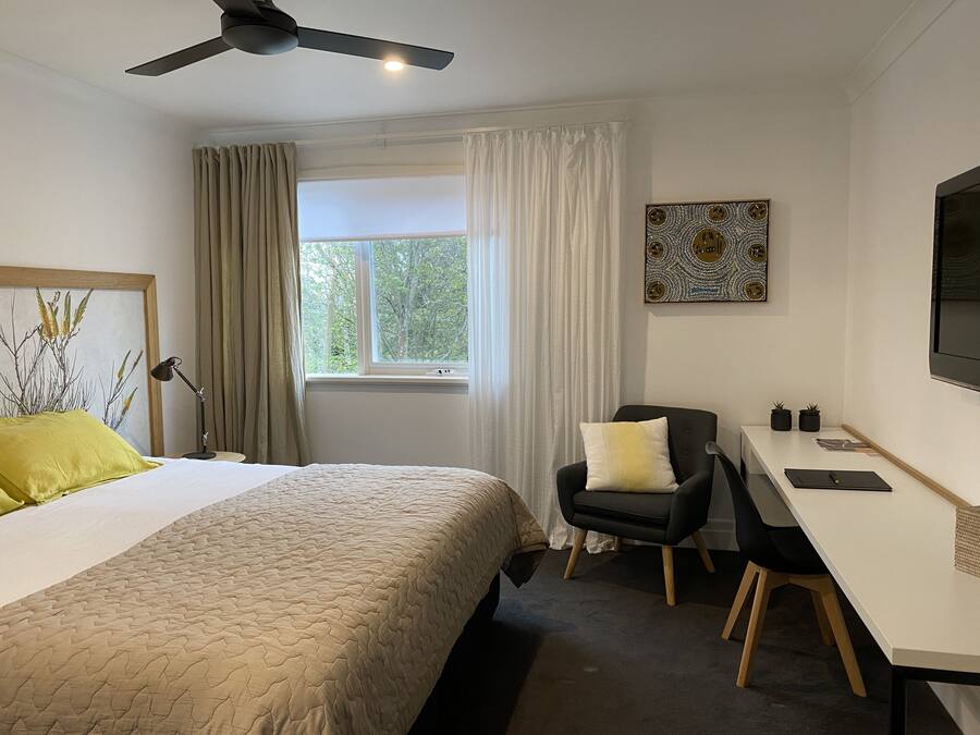 Ein Hotelzimmer mit Bett, Schreibtisch, Stuhl, Deckenventilator und einem Fenster mit Vorhängen.