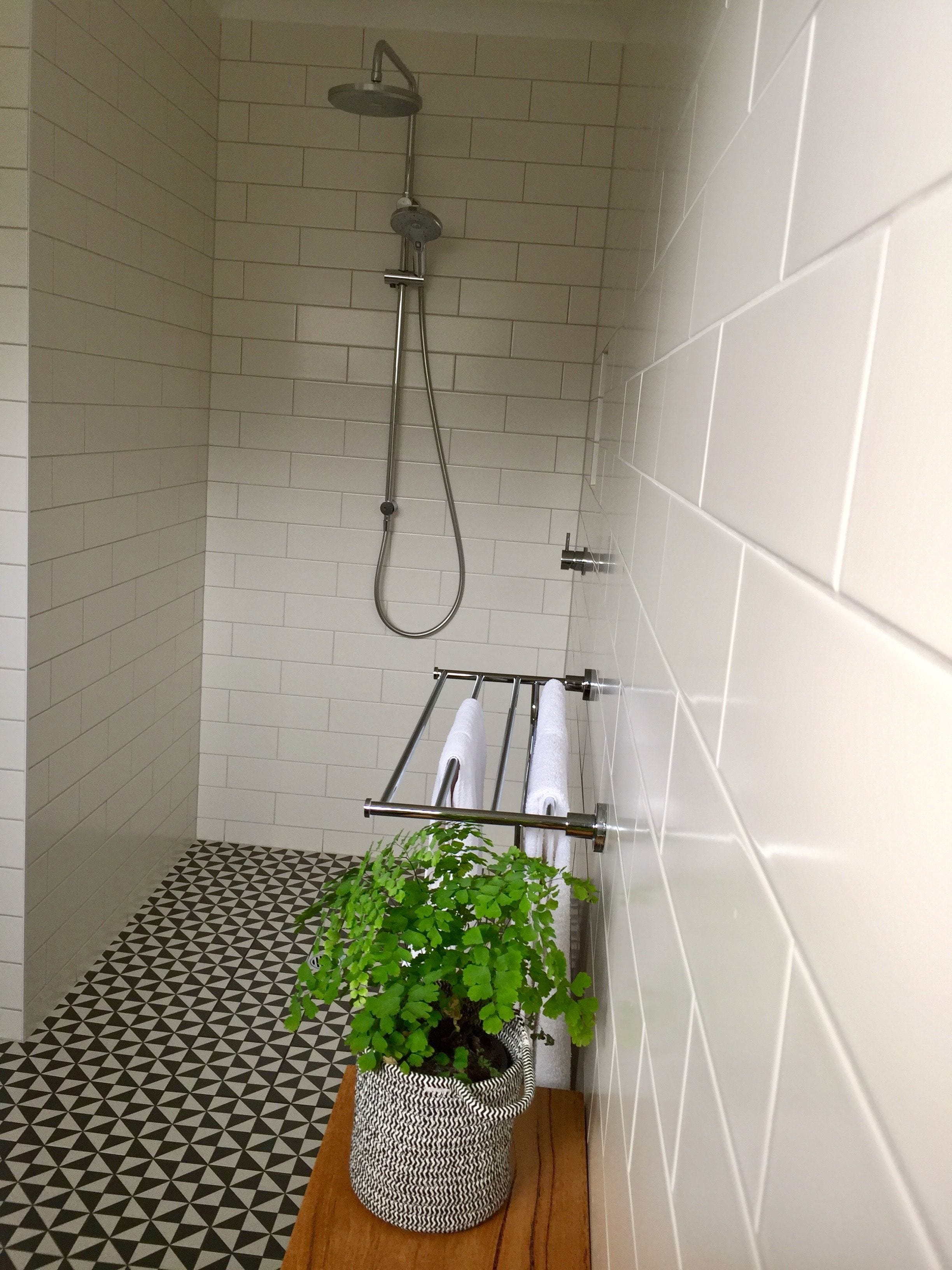 A shower area with white tiled walls, a black and white patterned floor, and a towel rack with white towels.