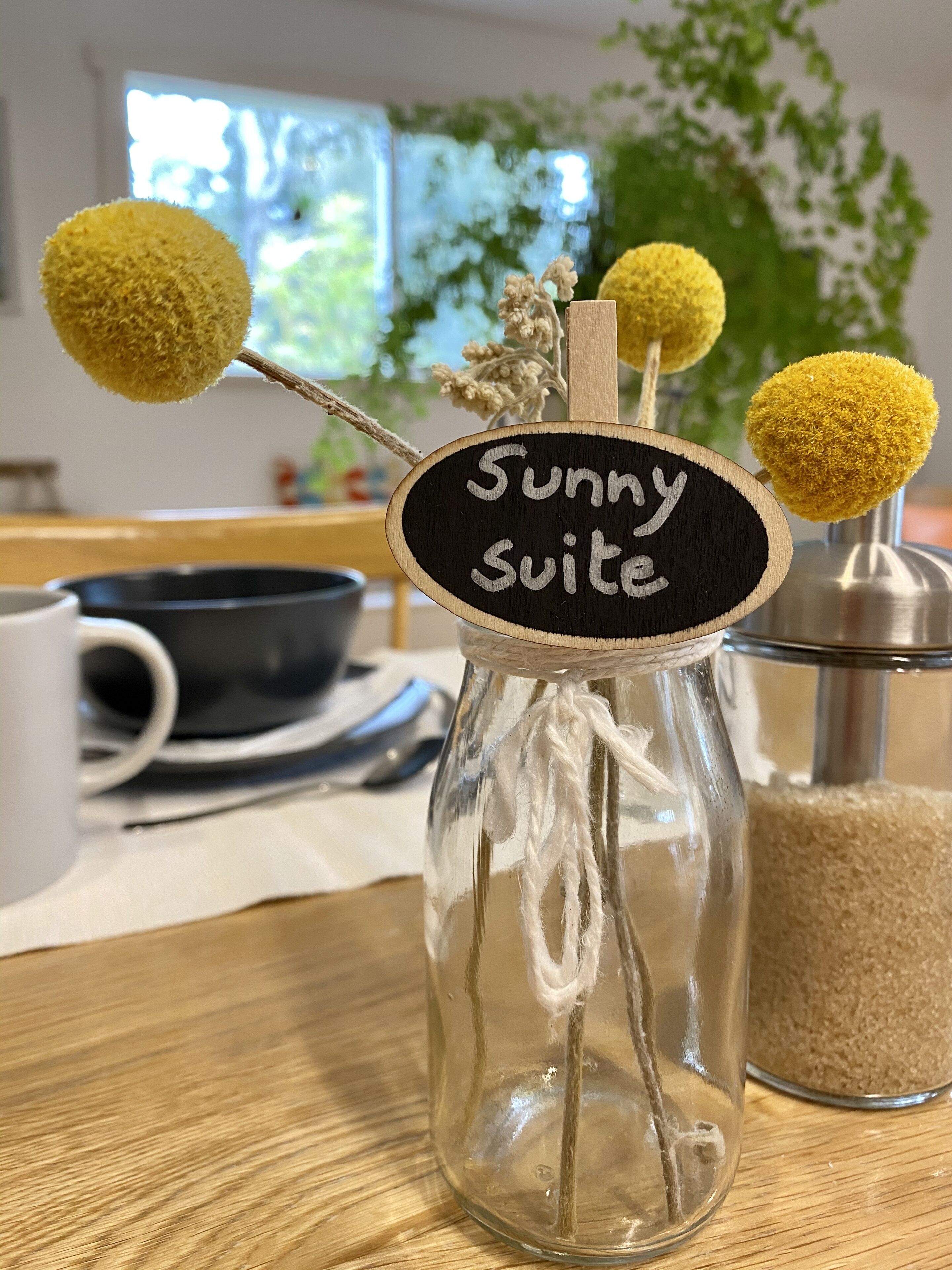 Eine klare Glasflasche mit dem Aufkleber "Sunny Suite" und dekorativen gelben Pompons.
