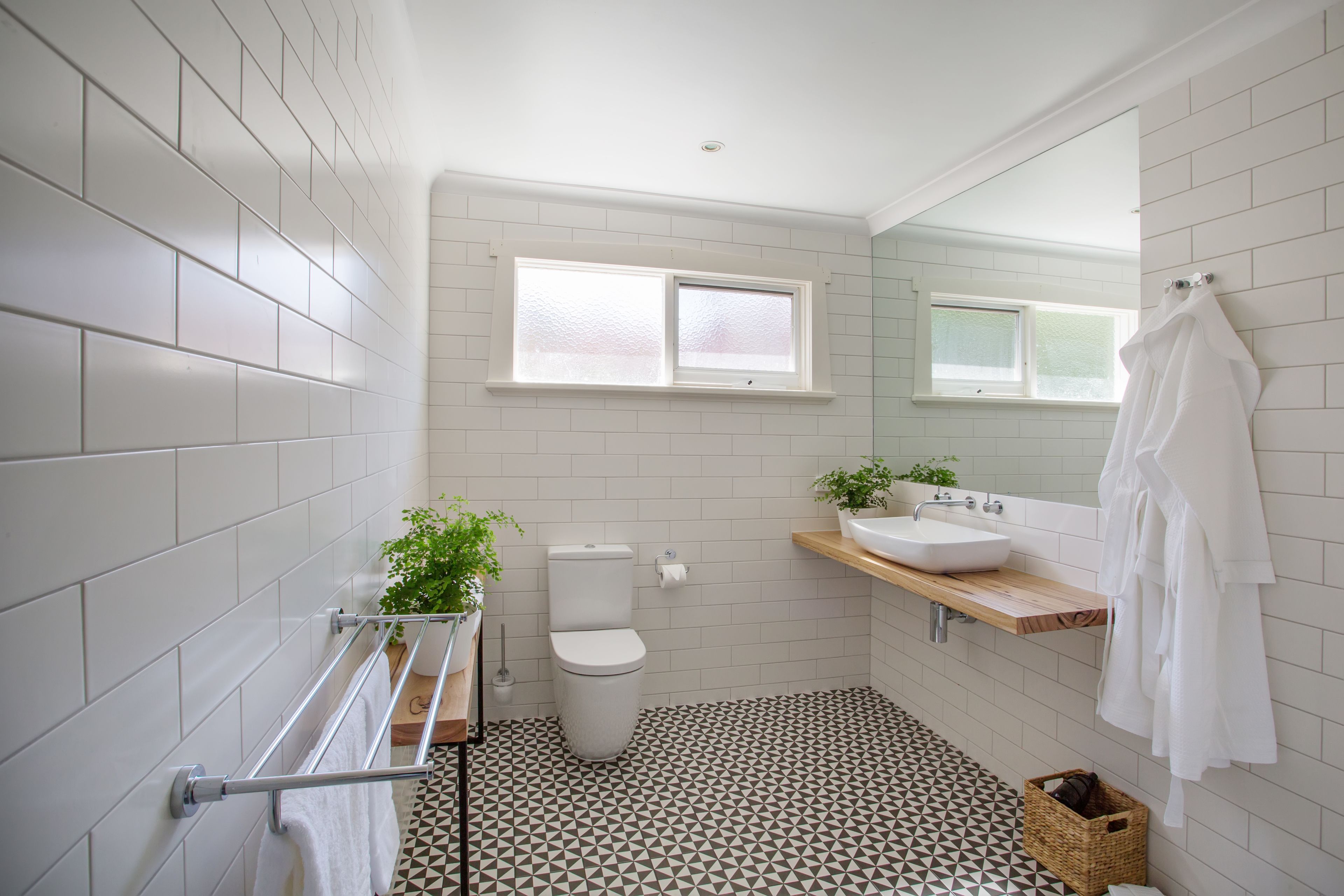 A bathroom with white tiled walls, a toilet, a sink, and a window.