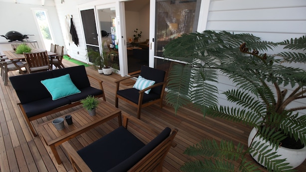 An outdoor deck with wooden furniture, including a sofa and chairs, and a large potted fern. - Sunny Side Up B&B (Rye)
