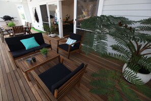 An outdoor deck with wooden furniture, including a sofa and chairs, and a large potted fern. - Sunny Side Up B&B (Rye)