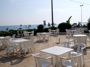 An outdoor seating area with white plastic tables and chairs, overlooking the sea.