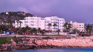 A coastal building complex with multiple white structures, palm trees, and a rocky shoreline. - Astreas Beach Hotel (Paralimni)