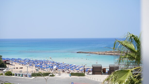A beach with numerous blue umbrellas and a clear view of the ocean. - Astreas Beach Hotel (Paralimni)