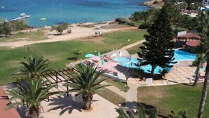 A resort with a pool area, palm trees, and a view of the sea. - Astreas Beach Hotel (Paralimni)