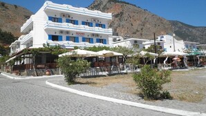 Edifici blanc amb detalls blaus, anomenat "ROOMS", que ofereix zones d'estar a l'aire lliure i un paisatge de muntanyes al fons.