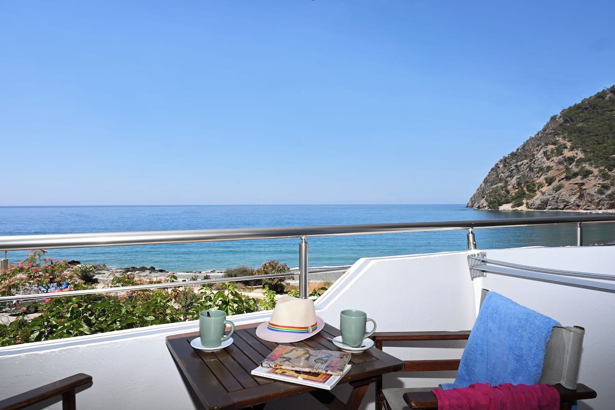 A balcony with a view of the sea, a table with a hat, two mugs, and a magazine.