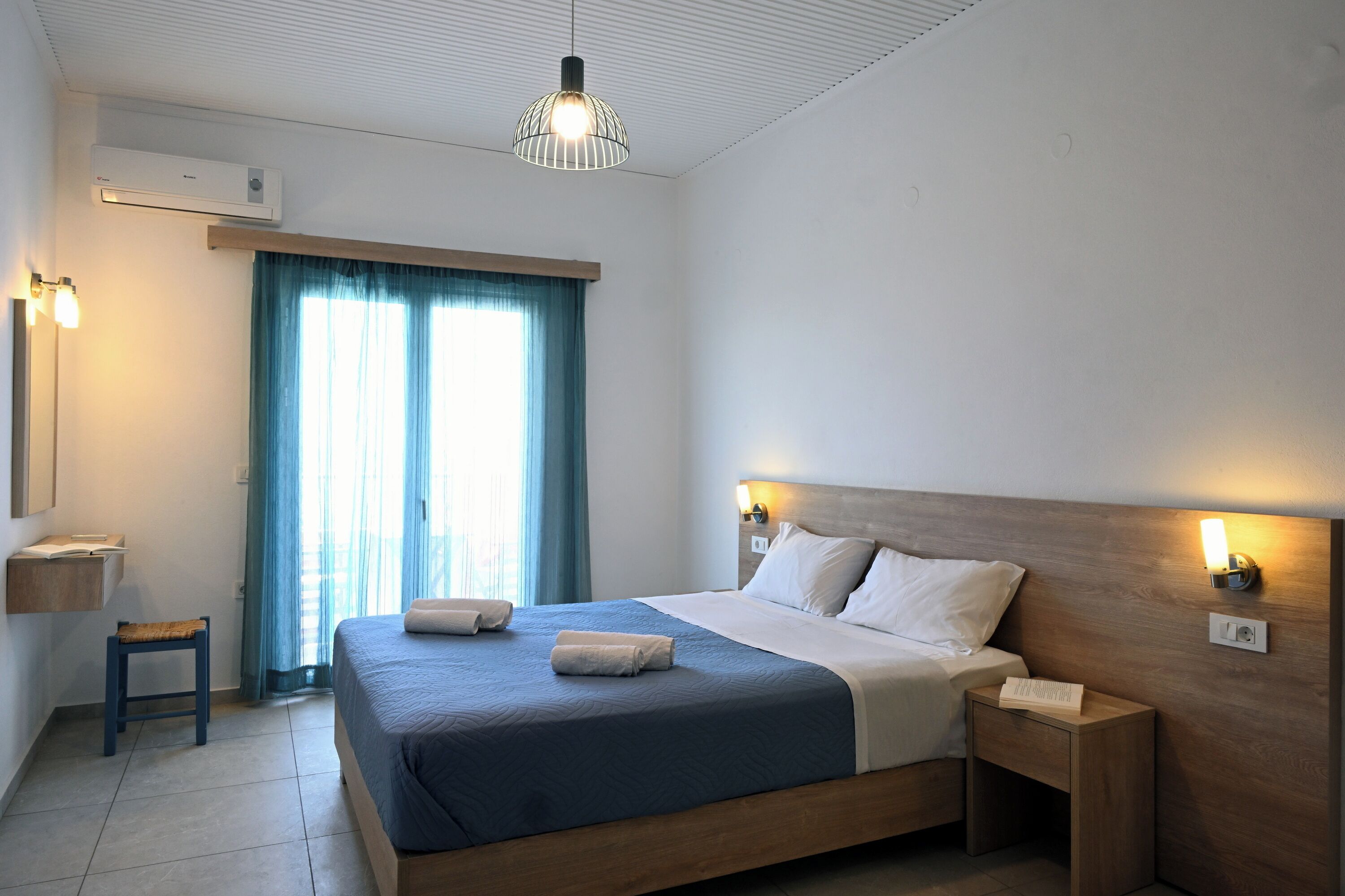 Ein modernes Hotelzimmer mit einem großen Bett, Nachttischlampen, einem kleinen Tisch und einem Fenster mit Vorhängen.