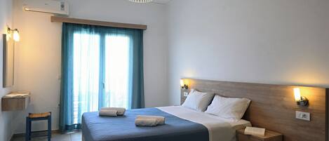 A modern hotel room with a large bed, bedside lamps, a small table, and a window with curtains.