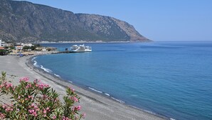 Paisatge costaner amb una platja, una embarcació i una muntanya al fons.