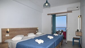 Habitació d'hotel amb un llit gran, dues taules de nit, un escriptori petit, una cadira i vista al mar a través d'una porta.