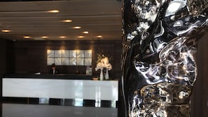 A modern reception area with a reflective sculpture, a counter, and a window with natural light. - WESTGATE Hotel (Taipei)