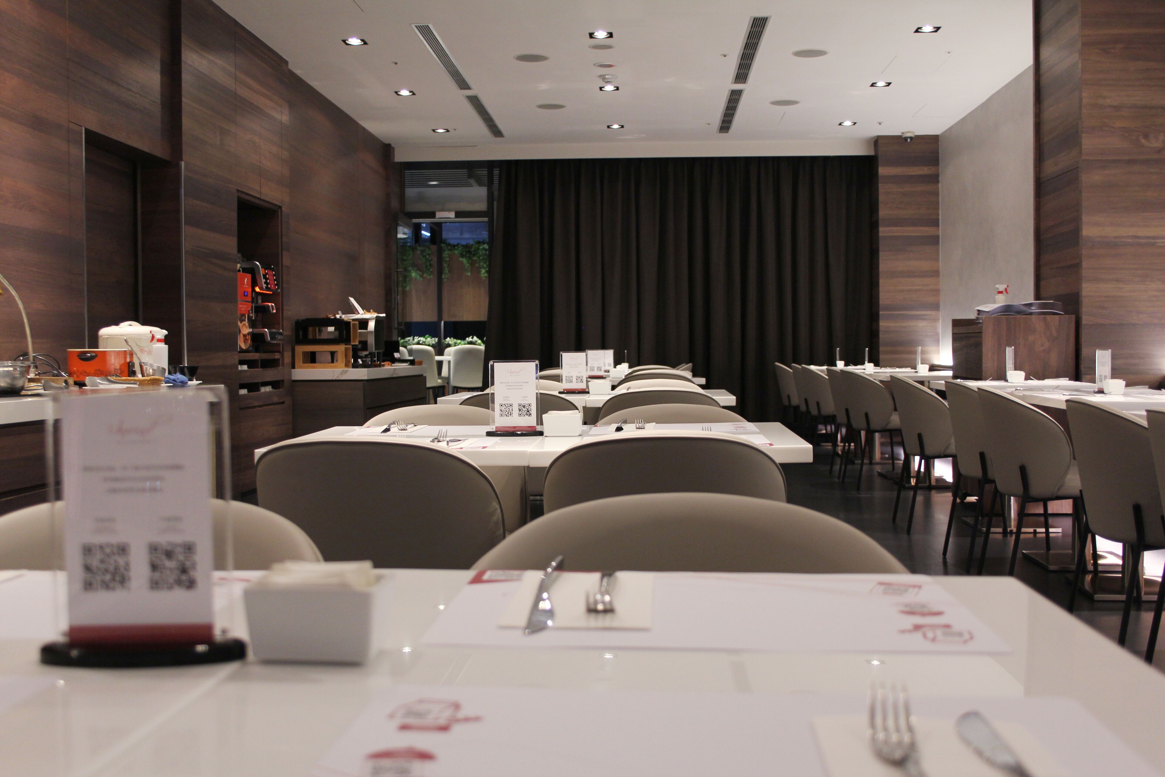 A modern dining area with tables set for service, a menu stand, and a counter with a cash register.