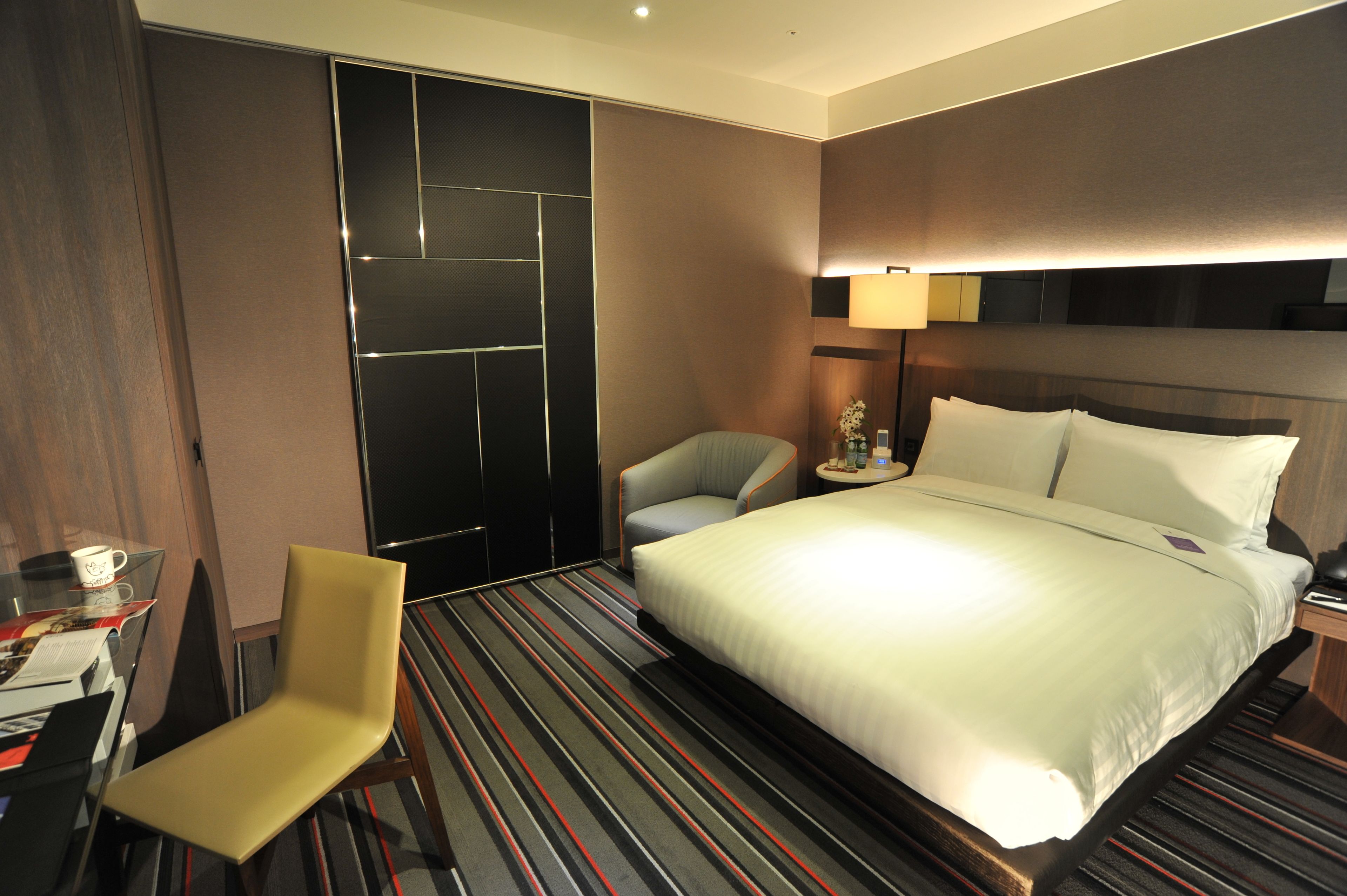 A hotel room with a large bed, a chair, a desk with a computer, and a wardrobe.