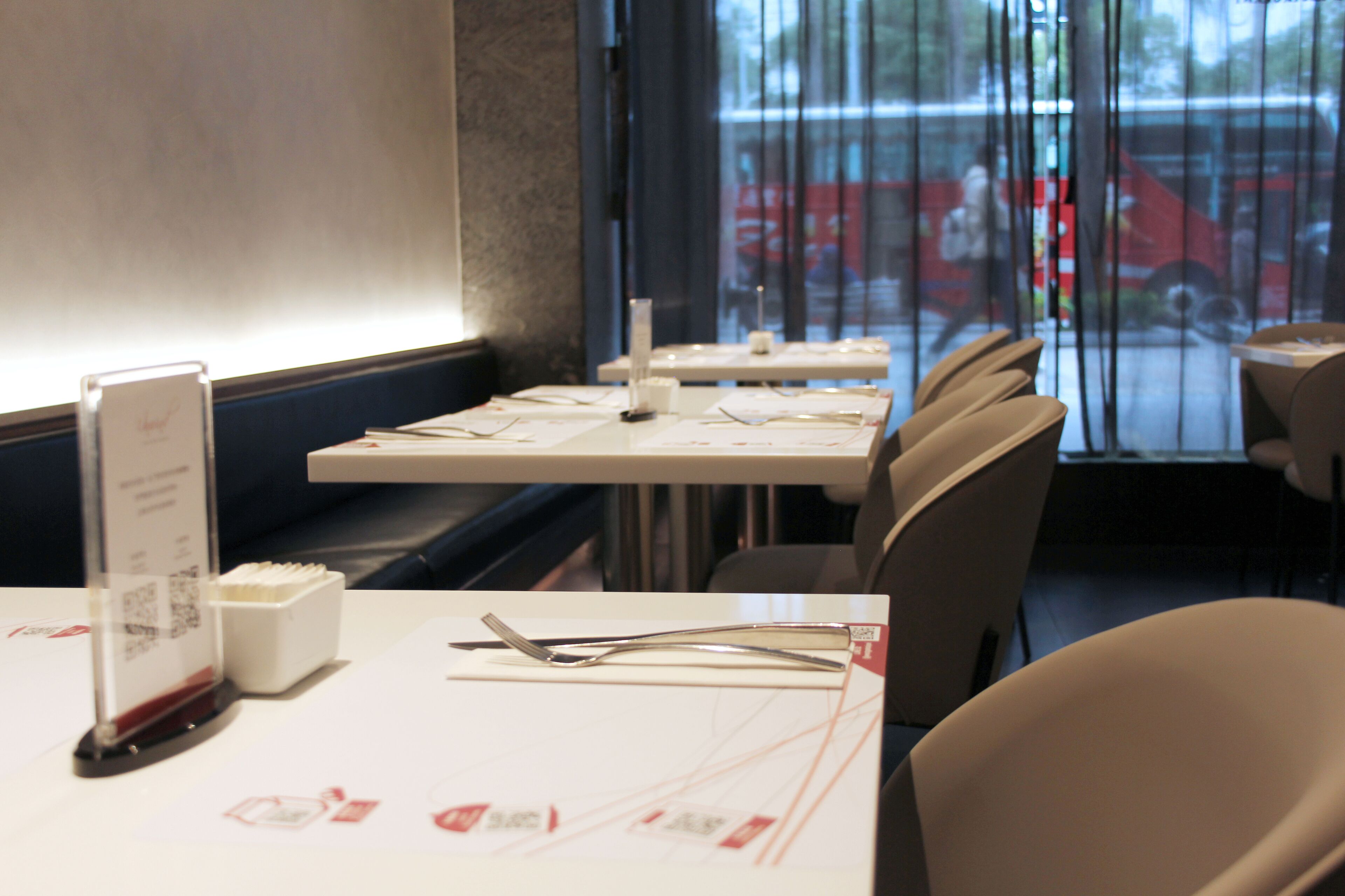 A restaurant interior with tables set for dining, a menu stand, and a view of the street through the window.