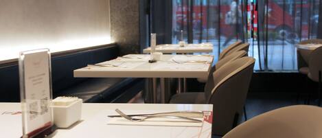 A restaurant interior with tables set for dining, a menu stand, and a view of the street through the window.