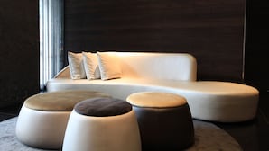 A modern living area with a sofa and ottomans, a dark wooden wall, and a large window with curtains. - WESTGATE Hotel (Taipei)