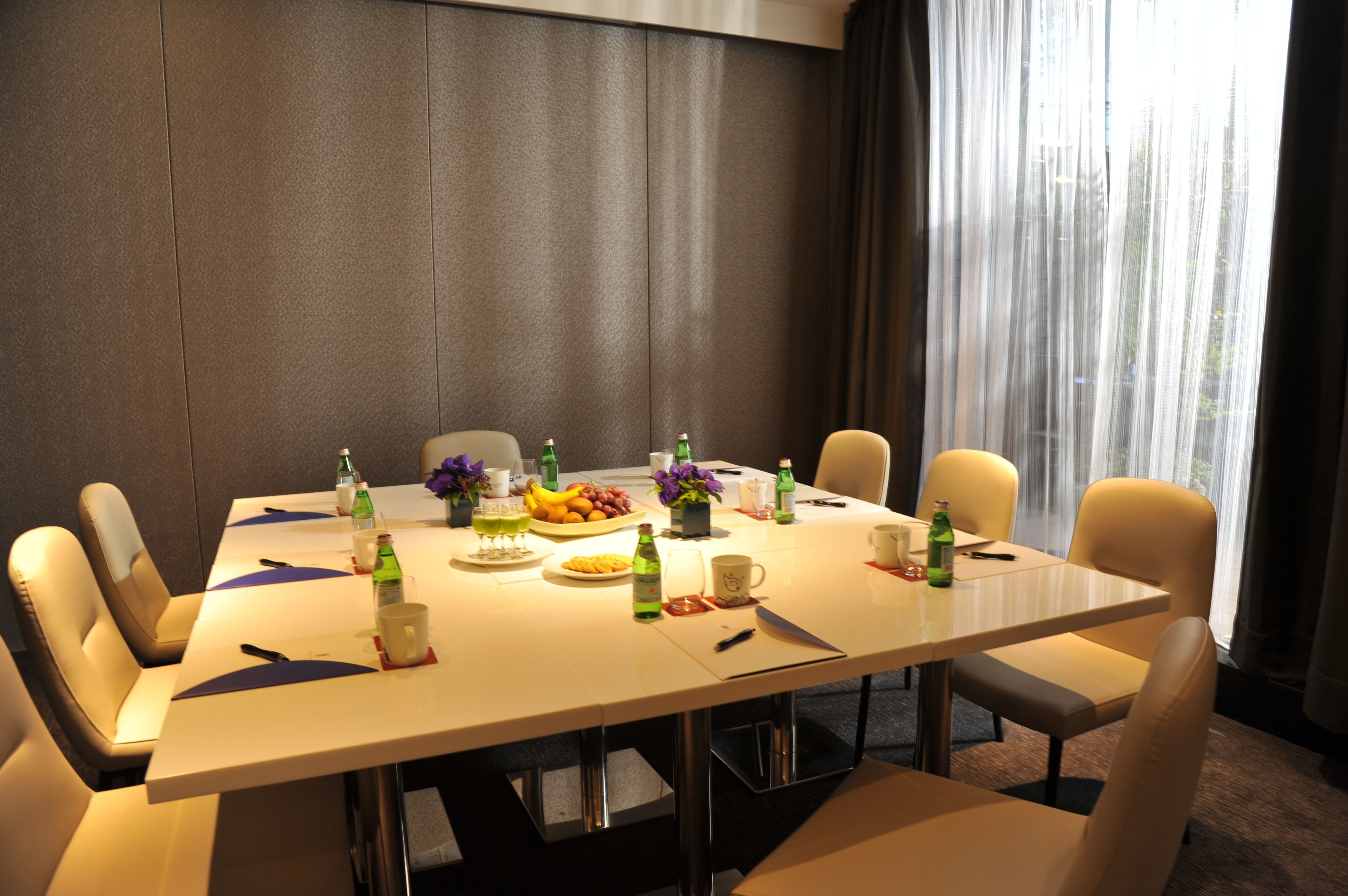 Een vergaderruimte met een lange tafel, stoelen en verschillende voorwerpen, zoals flessen, bekers en een schaal met fruit.