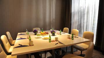 Een vergaderruimte met een lange tafel, stoelen en verschillende voorwerpen, zoals flessen, bekers en een schaal met fruit.