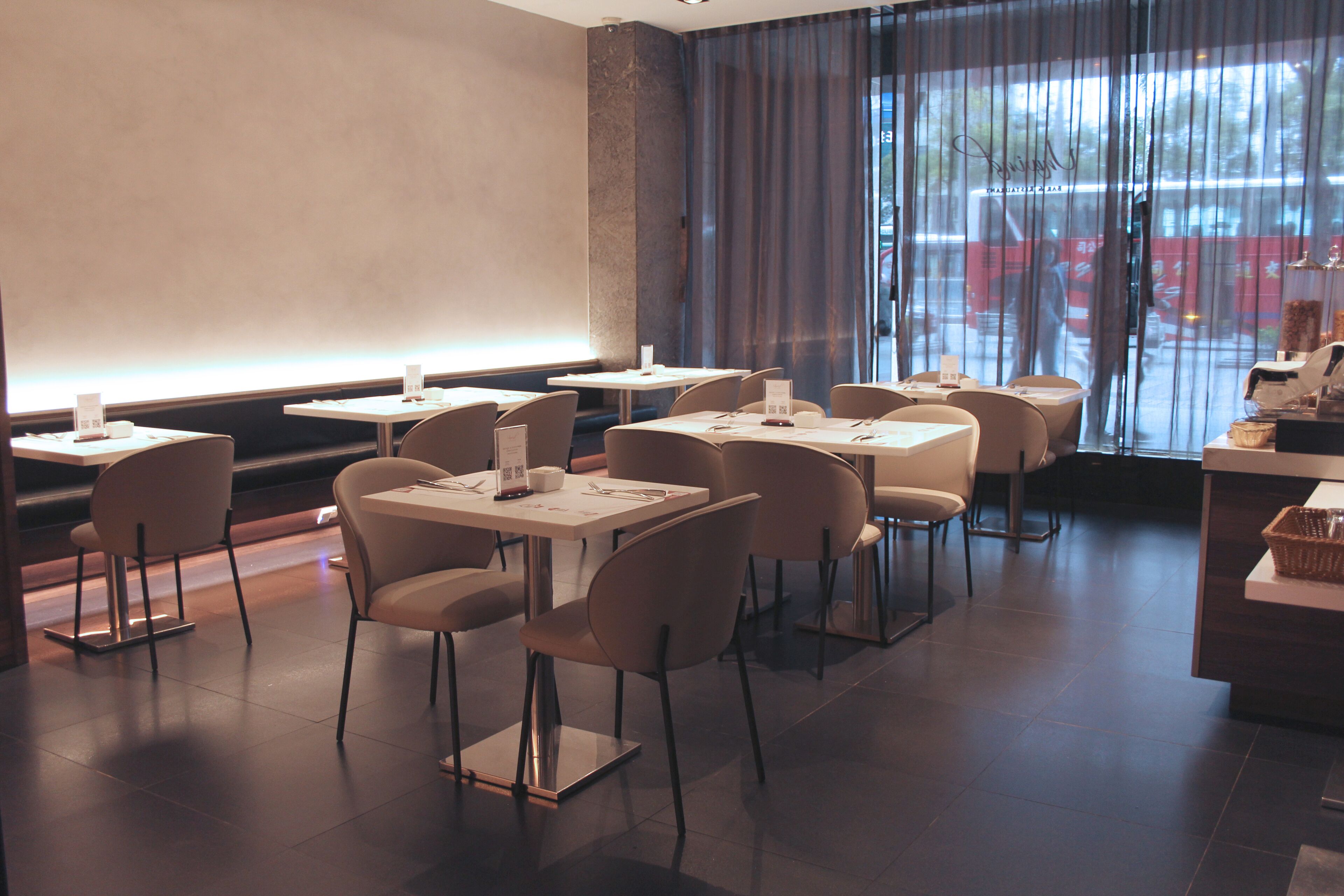 A modern restaurant with a clean, minimalist interior. Tables are arranged in a U-shape around a central bar area.