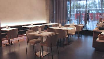 A modern restaurant with a clean, minimalist interior. Tables are arranged in a U-shape around a central bar area.