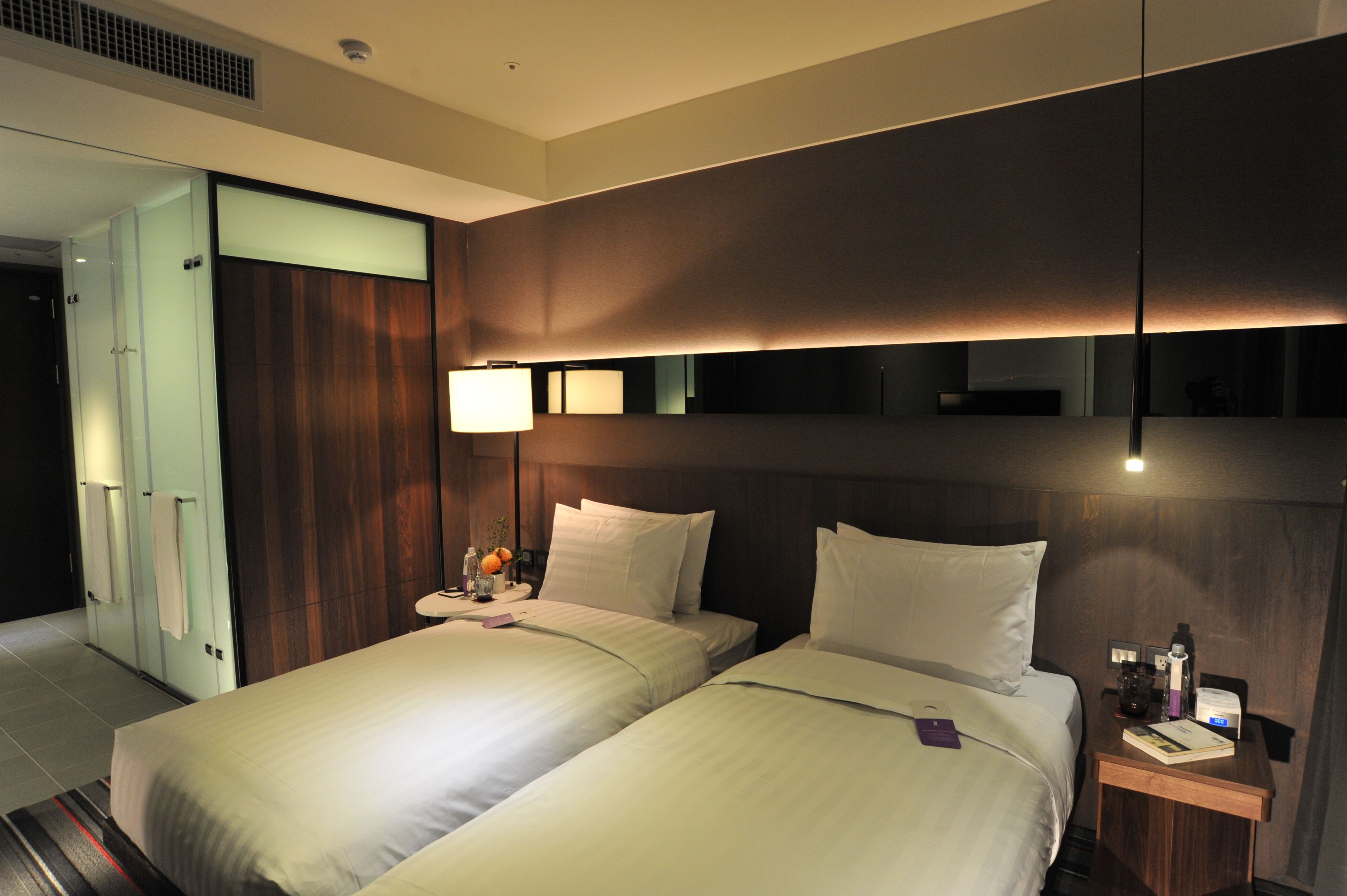 A hotel room with two beds, a wooden headboard, a nightstand with a lamp, and a mirror.