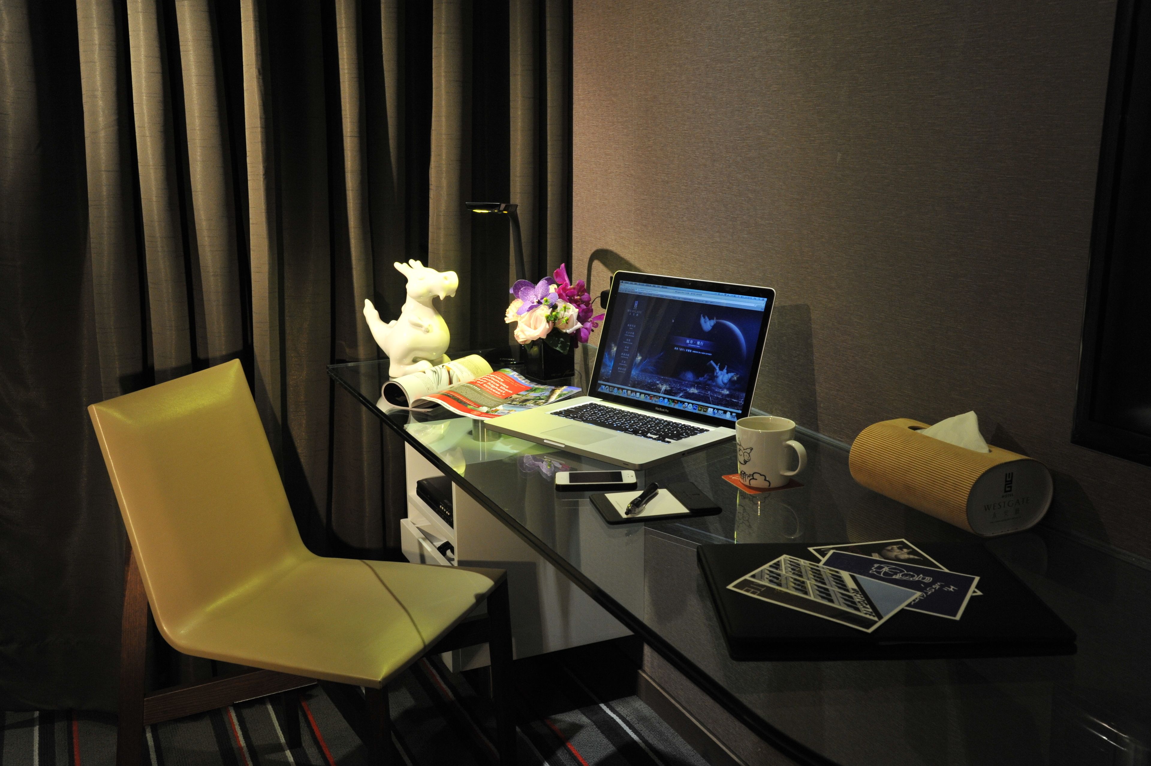 A hotel room with a glass desk, a laptop, a cup, a tissue box, and a chair.