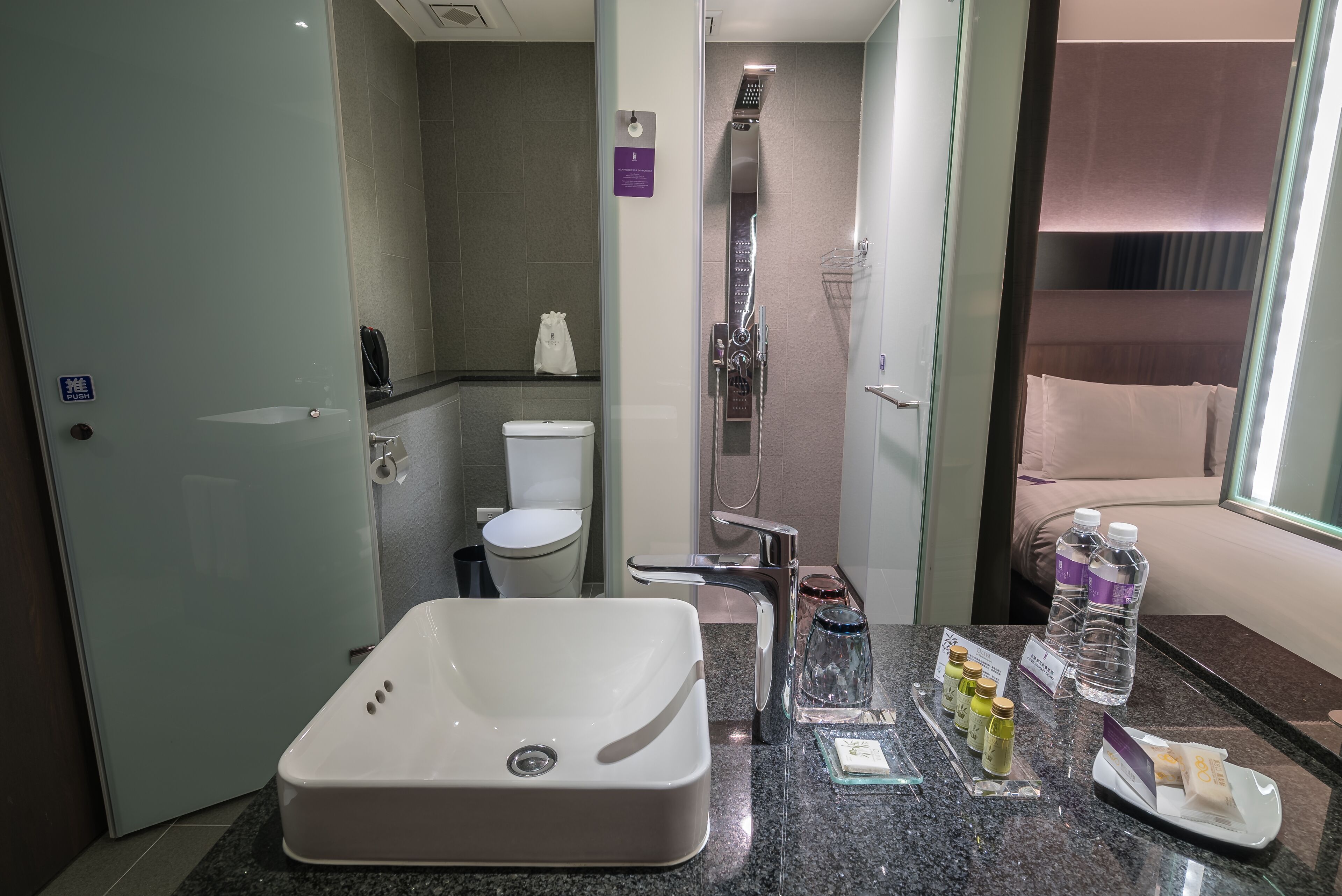 Un baño de hotel con una bañera grande, un inodoro, una ducha y un lavabo. Hay artículos de aseo en el mostrador.