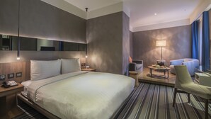 A modern hotel room with a large bed, bedside tables, a desk, a chair, a lamp, and a view of the city. - WESTGATE Hotel (Taipei)