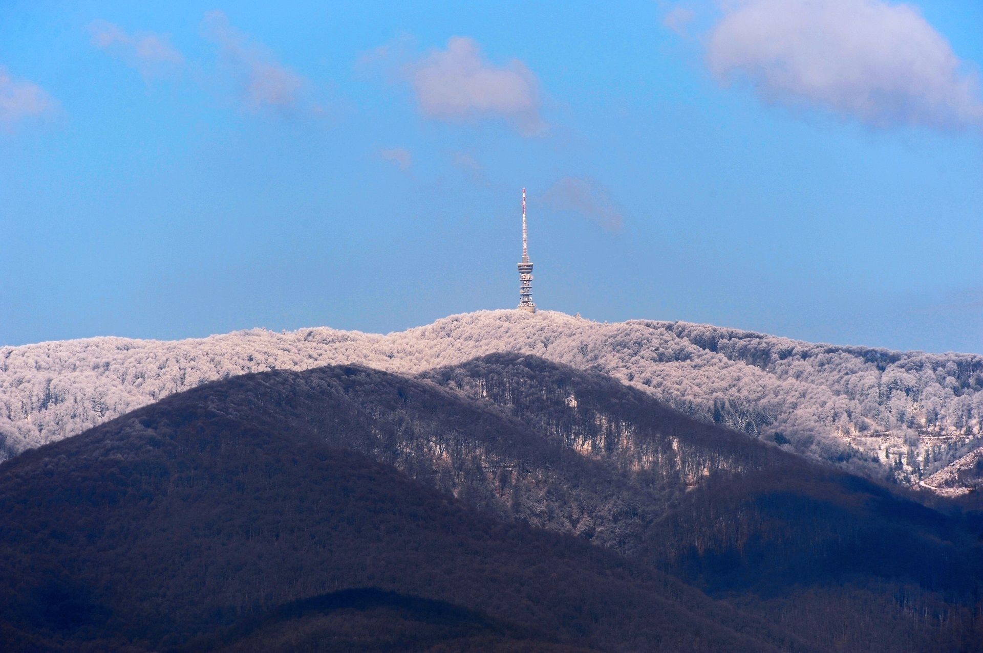 Ein Turm auf einem mit Schnee bedeckten Hügel vor blauem Himmel.