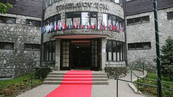 Un edificio de piedra con una alfombra roja que conduce a la entrada, banderas y el nombre "DOMISLAVOV DOM".
