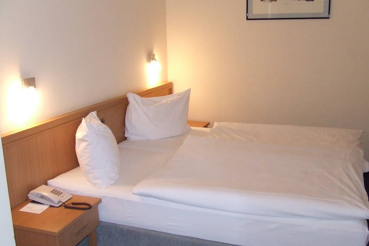 A neatly made bed with white linens, a wooden headboard, and a bedside table with a telephone and papers.