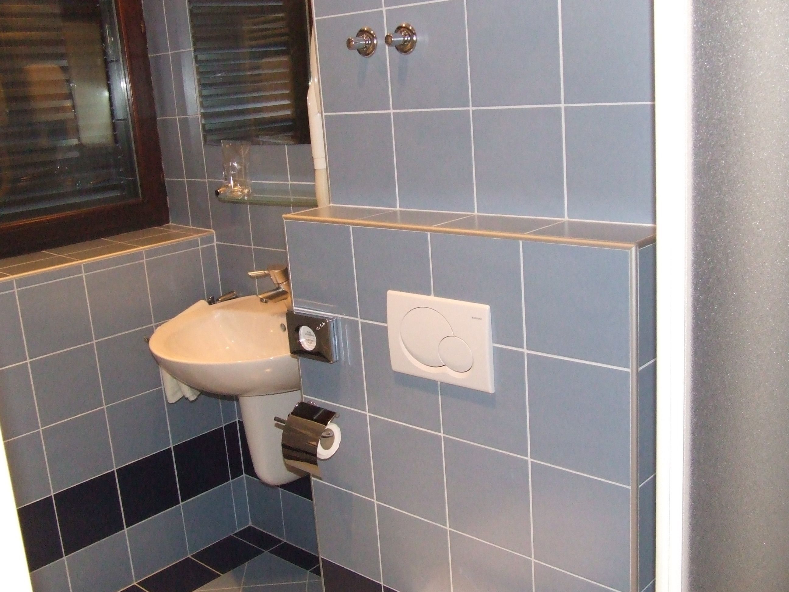 A bathroom with a sink, toilet paper holder, and a hand dryer.