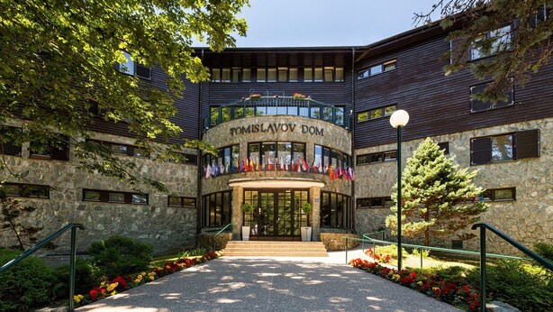 A stone building with a central entrance, surrounded by a landscaped garden with red and yellow flowers. - Hotel Tomislavov Dom (Zagreb)