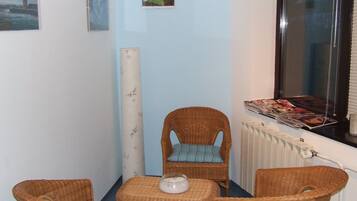 A corner room with a wicker chair, a small table, and a window with a magazine rack.