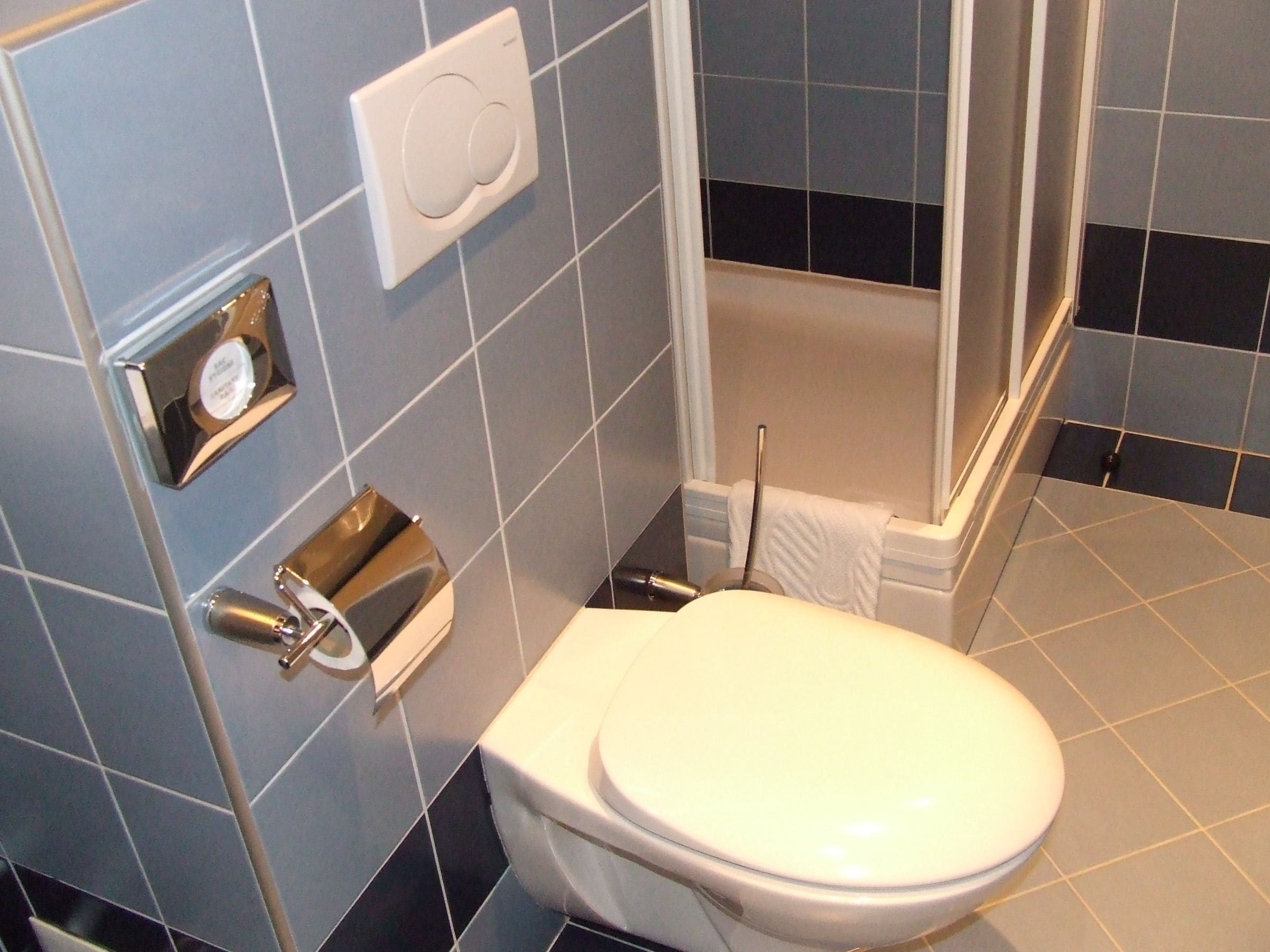 Un baño con inodoro, toallero, secador de manos y dispensador de papel higiénico.