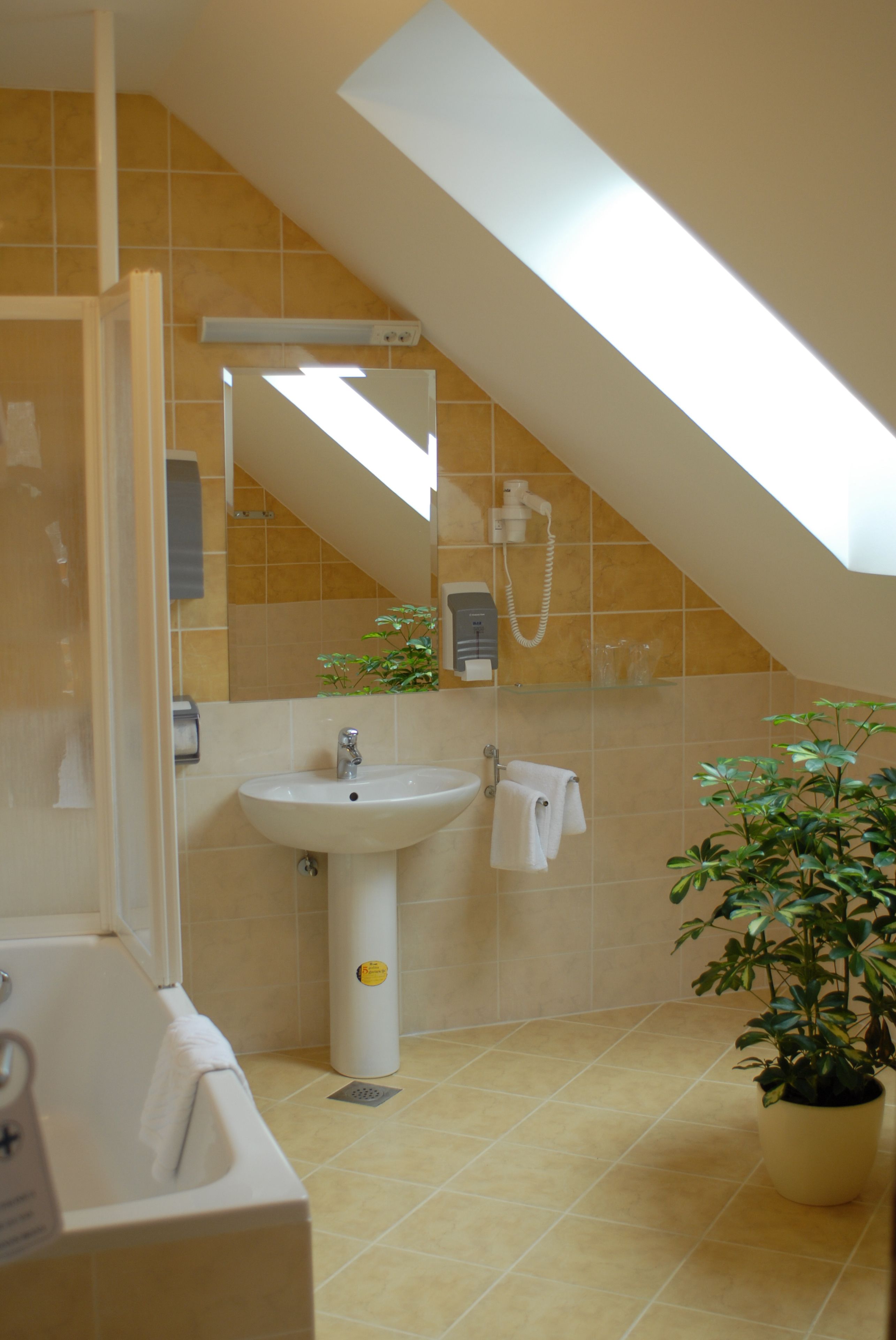 Un baño con tragaluz, lavabo, espejo, toallero y planta en maceta.