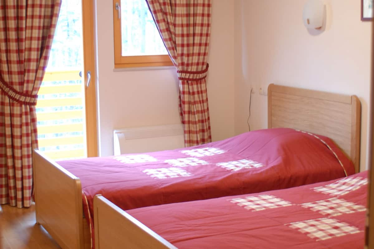 A room with two wooden beds, red bedding, checkered curtains, a window, and a radiator.