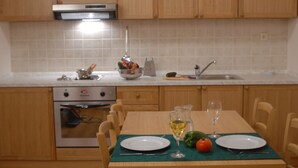 A kitchen with wooden cabinets, a stove, and a dining table set with plates, a glass of wine, and vegetables. - Aparthotel Snjezna Kraljica (Stubicke Toplice)