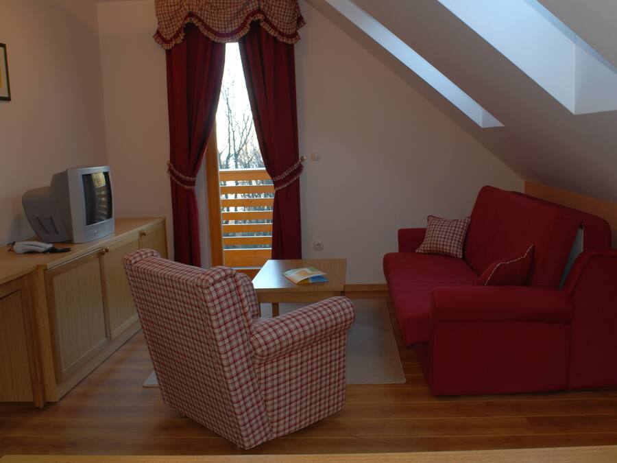 A cozy living room with a red sofa, a checkered armchair, a small table with a book, and a television on a wooden cabinet.