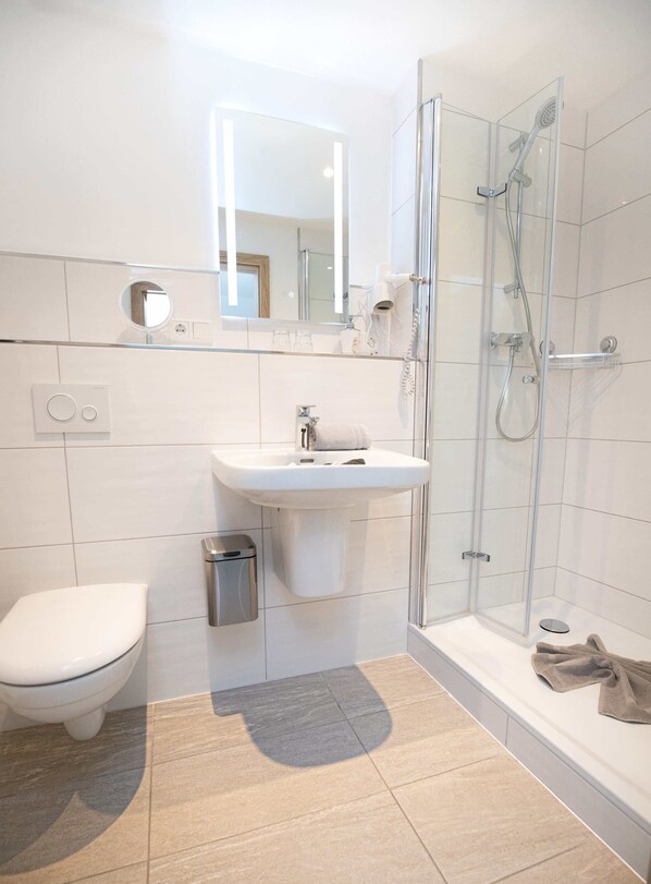 A modern bathroom with a toilet, sink, and glass-enclosed shower. - Hotel Restaurant Amadeus (Bad Hindelang)