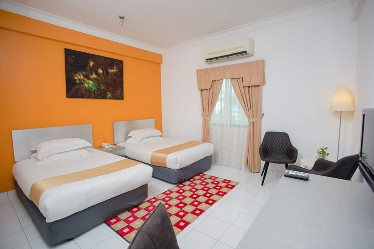 Een hotelkamer met twee bedden, een bureau, een stoel, een airconditioner en een schilderij aan de muur.
