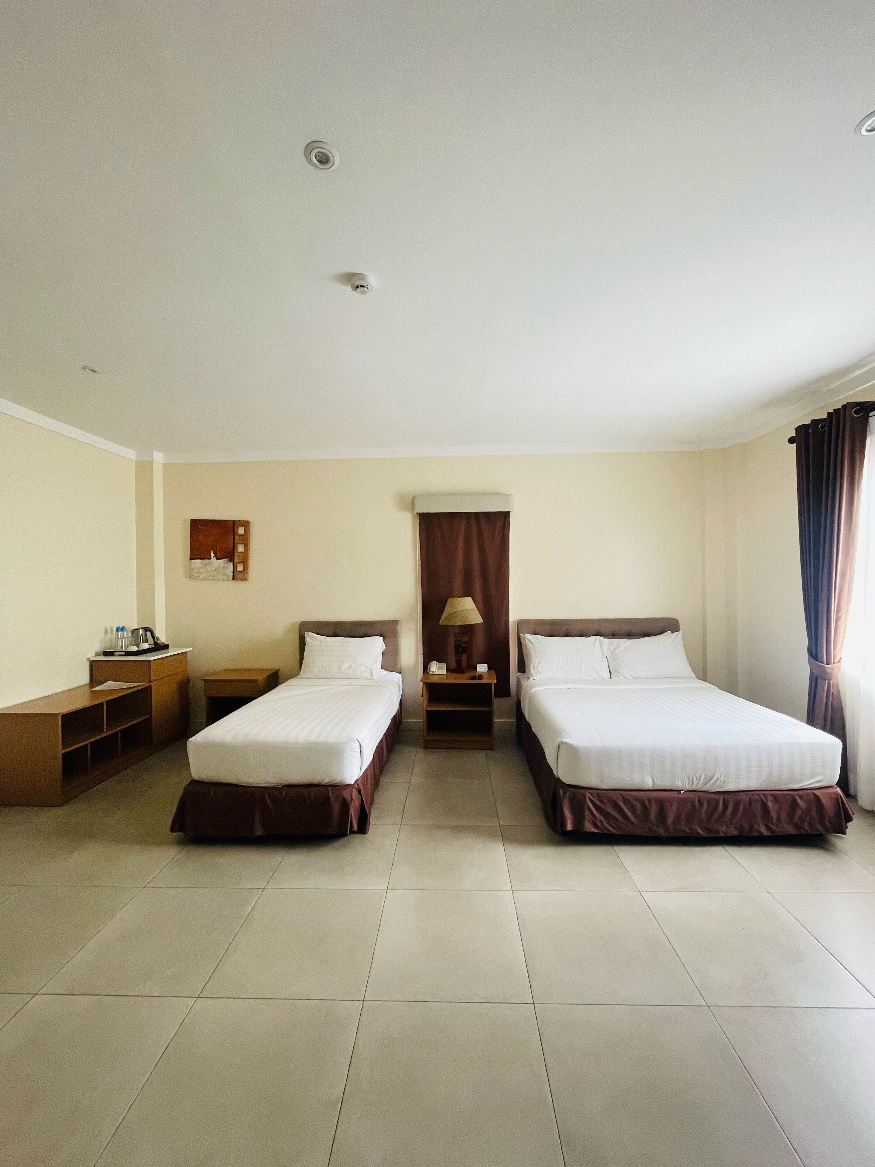 A hotel room with two beds, a desk, a lamp, and a small table.