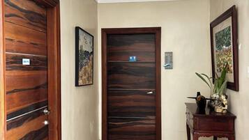 A hallway with a wooden door on the left, a framed picture on the wall, and a small table with a plant on the right.